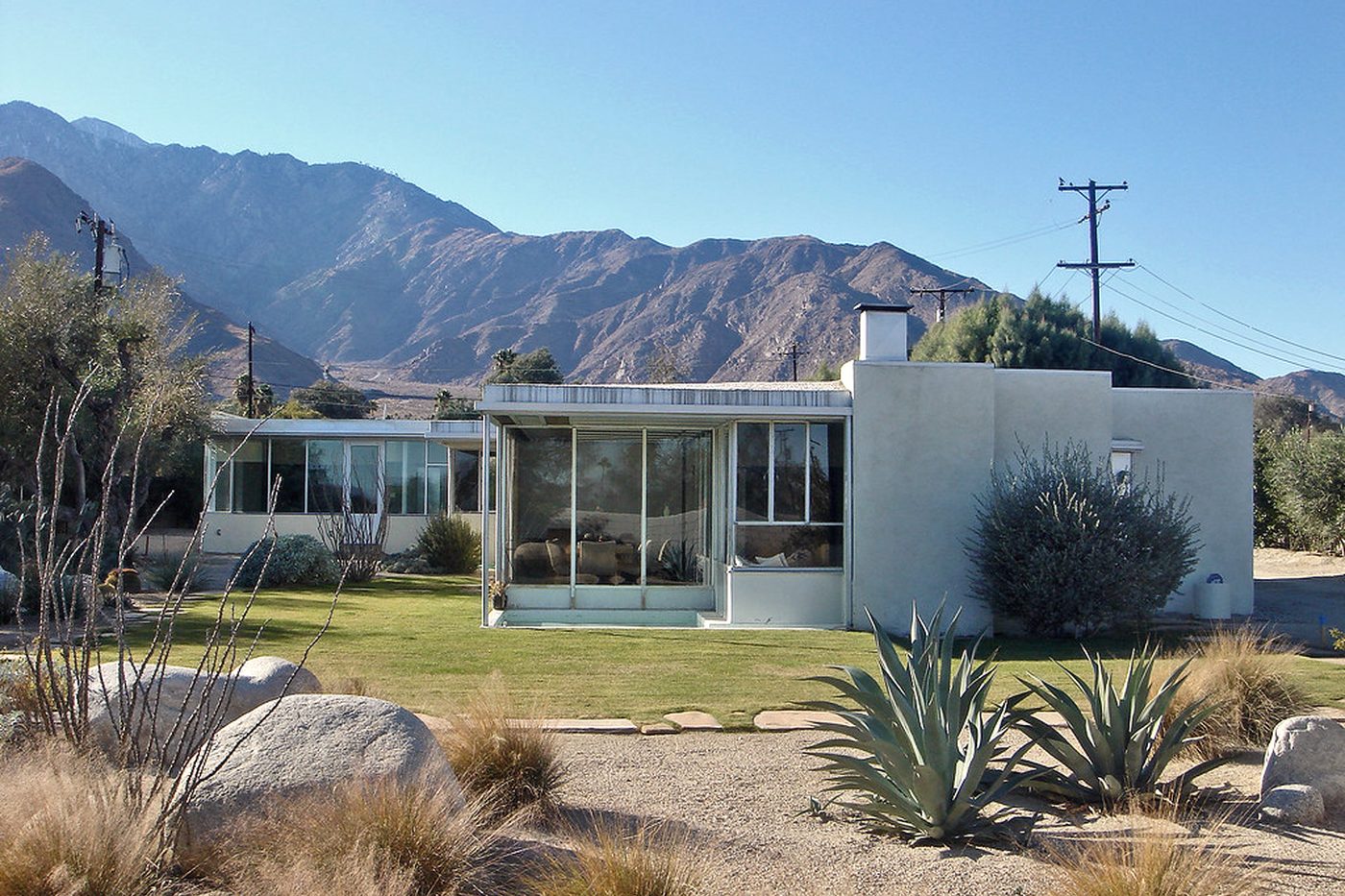 A mid-century modern desert house with a low-water landscape of agave, boulders and desert grasses.